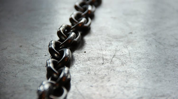 Photograph of a black metal chain on a rough grey surface.