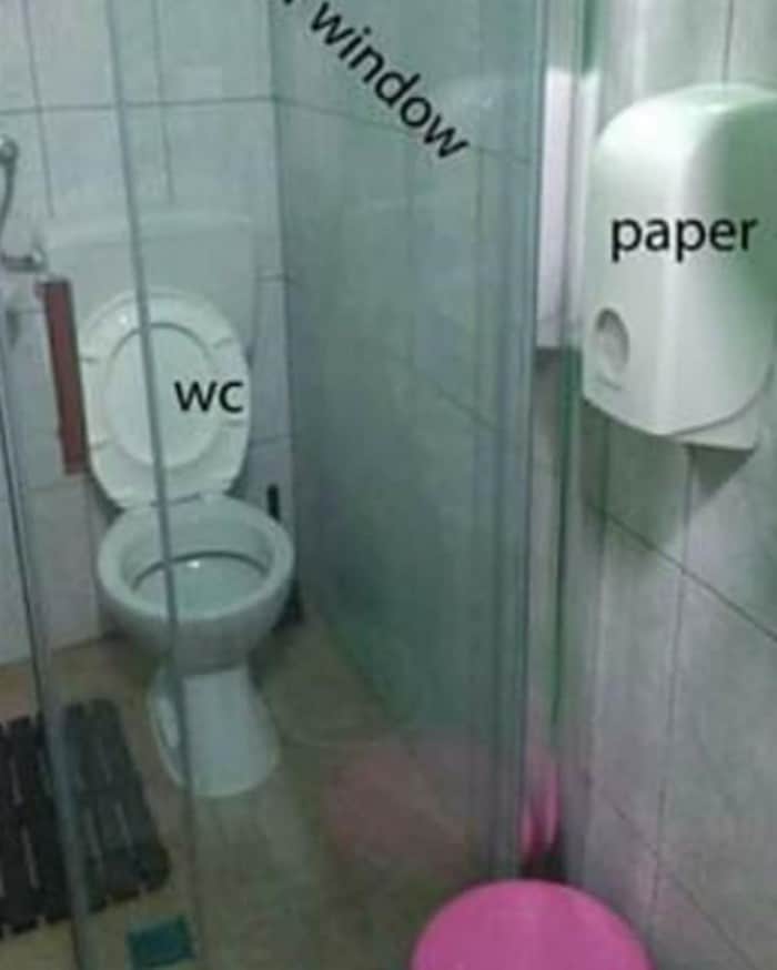 Photograph of a WC with a glass door separating the WC from the toilet paper holder.