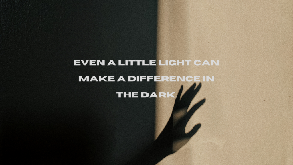 A person reaching out in a room with poor light. The caption on the image reads, "Even a little light can make a difference in the dark." The caption is written in light colours, making it easier to read against the dark background than the previous image.