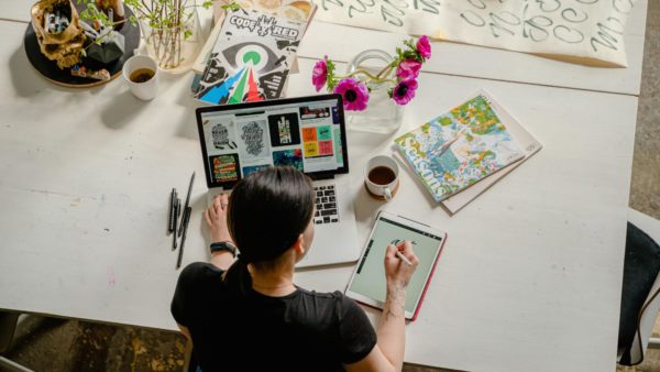 Person drawing on a tablet while looking at a moodboard on a laptop