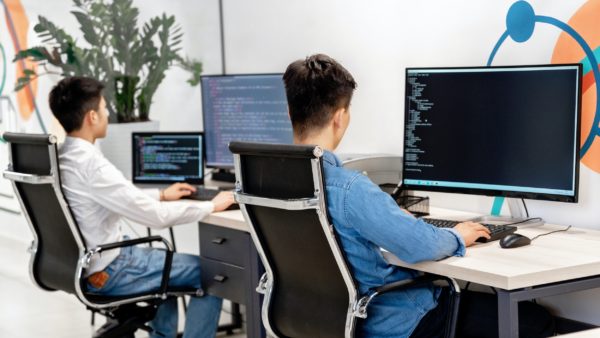 Two people sitting in front of large-screen monitors showing lines of code.